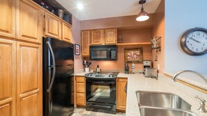 A kitchen with wooden cabinets, a stainless steel refrigerator, a microwave, an oven, a sink, and a clock on the wall.