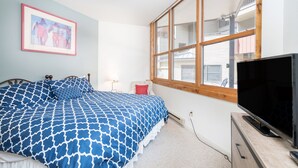 Une chambre à coucher avec un lit, une télévision, une fenêtre et un tableau encadré au mur.