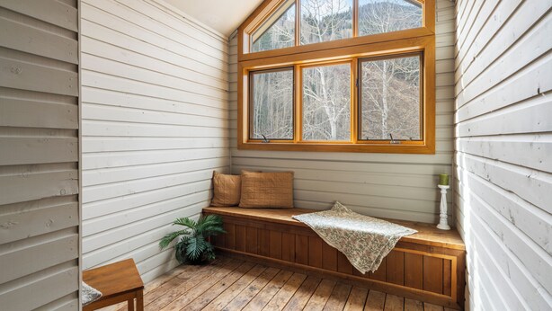 Un rincón acogedor con un banco de madera, una mesita y una ventana con vistas a los árboles.