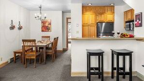 Una cocina moderna con armarios de madera, un refrigerador de acero inoxidable y una barra con taburetes.