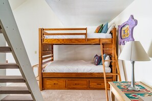 Una cama litera con estructura de madera, colchón blanco y una mesita de noche con lámpara.
