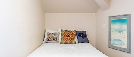 A bed with three pillows, a framed picture on the wall, and a light switch.