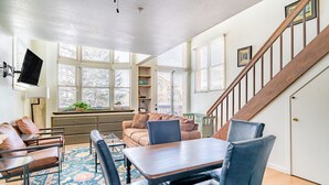 A spacious living room with a wooden staircase, a dining area with a table and chairs, and a cozy seating area with a sofa and cushions. - Columbia Place 5 by AvantStay | Ski-In/Ski-Out Unit in Great Location! (Mountain Village)