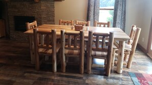 A dining area with a stone fireplace, wooden chairs, a wooden table, and a window with curtains. - Mountain View Retreat - on 5 private acres only 6 miles from Ohiopyle (Mill Run)