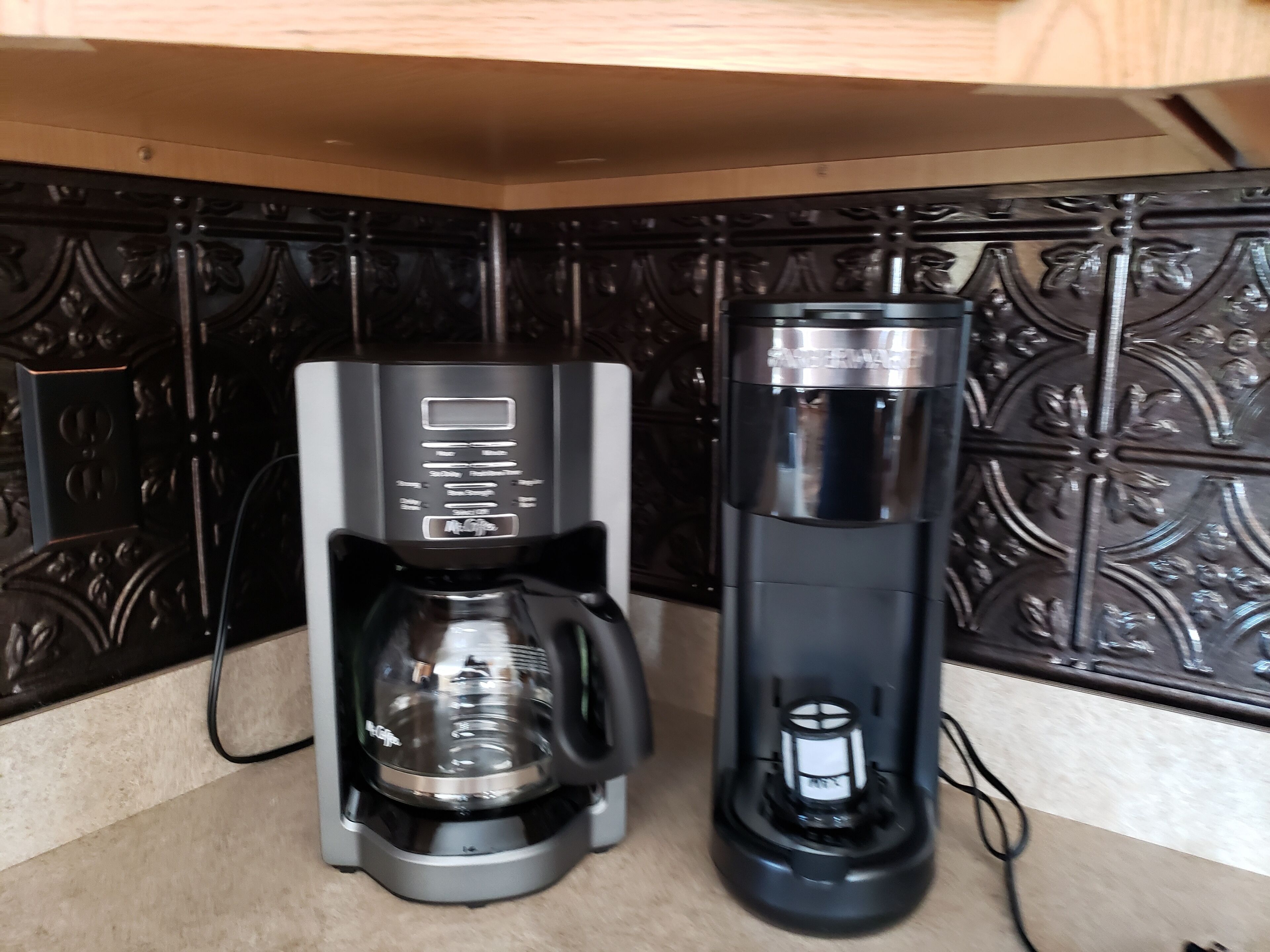 Una cafetera y un dispensador de agua sobre una encimera de cocina con baldosas negras decorativas.