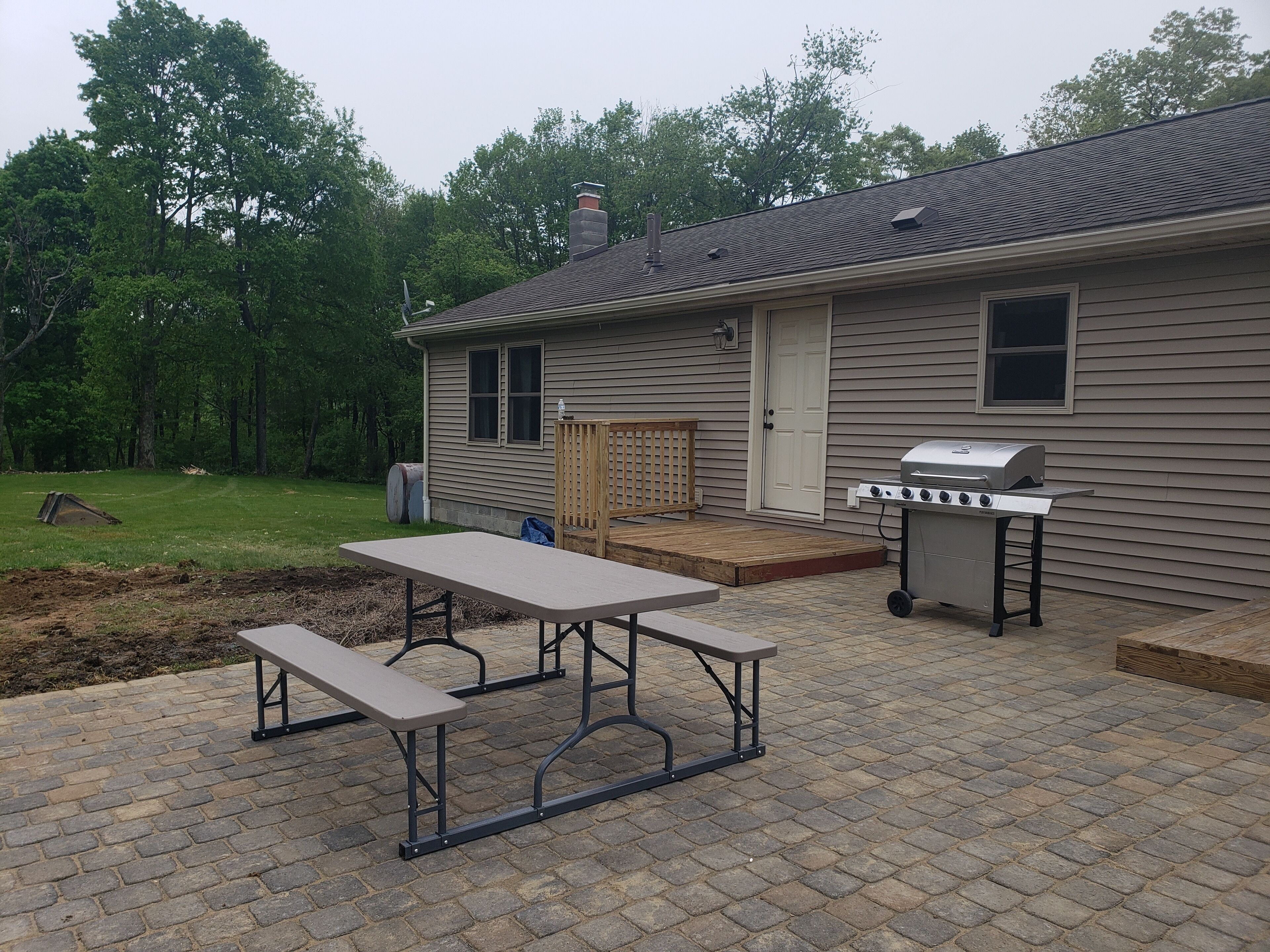 A patio with a picnic table and a grill outside a house.