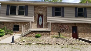 A two-story building with a stone facade, a front porch with a railing, and a small front yard with gravel and plants. - Mountain View Retreat - on 5 private acres only 6 miles from Ohiopyle (Mill Run)