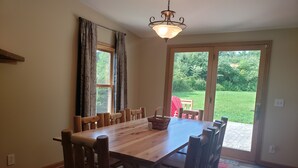 A dining area with a wooden table and chairs, a chandelier, and a view of a garden through a sliding glass door. - Mountain View Retreat - on 5 private acres only 6 miles from Ohiopyle (Mill Run)