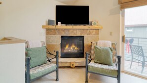 Una sala de estar con chimenea, dos sillones y un televisor sobre la chimenea.