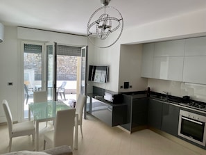 A modern kitchen with a built-in oven and a dining area with a glass table and white chairs.