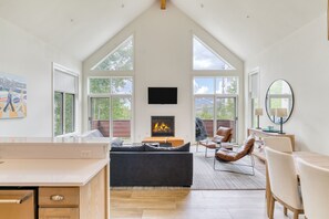 A spacious living room with a fireplace, large windows, a flat-screen TV, and a dining area.