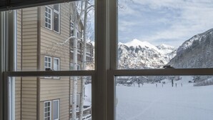 Näkymä rakennuksen ikkunasta, josta avautuu lumipeitteinen maisema ja taustalla kohoavat vuoret.
