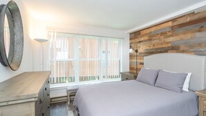 Quarto com cama, penteadeira, luminária e janela com persianas.