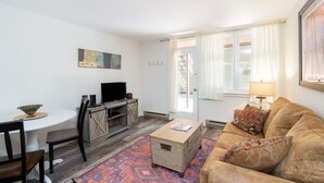 Uma sala de estar com sofá, mesa de centro, televisão e um espaço de jantar com cadeiras e mesa.