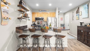 A modern kitchen with wooden cabinets, a stainless steel refrigerator, and a bar area with stools. - Etta Place 6 by AvantStay | Ski In/ Ski Out Unit! (Telluride)