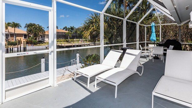 Ein überdachter Außenbereich mit weißen Lounge-Sesseln und Blick auf einen Pool.