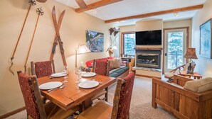 A cozy living room with a fireplace, a dining area with wooden furniture, and a TV mounted on the wall. - Ghostriders 5 by AvantStay | 2 Bedroom Condo Near Main Street, Hiking & Skiing | (Telluride)