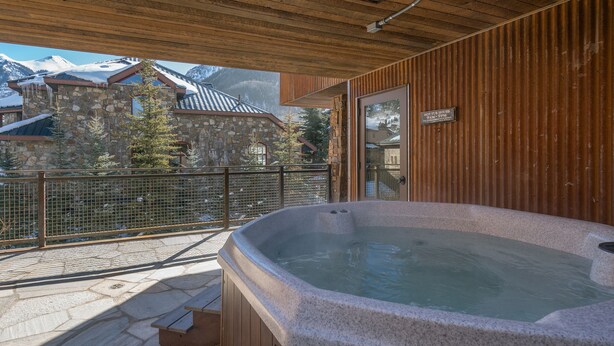 A hot tub on a wooden deck with a stone building in the background. - Ghostriders 5 by AvantStay | 2 Bedroom Condo Near Main Street, Hiking & Skiing | (Telluride)