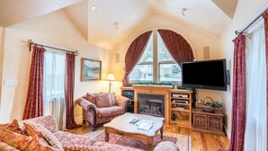 A cozy living room with a fireplace, a sofa set, a television, and a large window with curtains. - Hruza Hideout by AvantStay | Walkable Location + Free Ski Shuttle, Mountain View (Telluride)