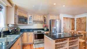 A kitchen with wooden cabinets, stainless steel appliances, a wine rack, and a sink. - Hruza Hideout by AvantStay | Walkable Location + Free Ski Shuttle, Mountain View (Telluride)
