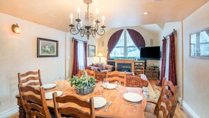 A dining area with a wooden table set for six, surrounded by wooden chairs. A chandelier hangs from the ceiling, and a television is visible in the background. - Hruza Hideout by AvantStay | Walkable Location + Free Ski Shuttle, Mountain View (Telluride)