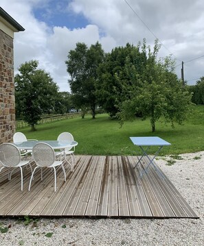 Um deck de madeira com mobiliário externo, gramado e árvores.