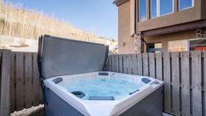 Un jacuzzi en un entorno exterior con una valla de madera y un edificio al fondo.