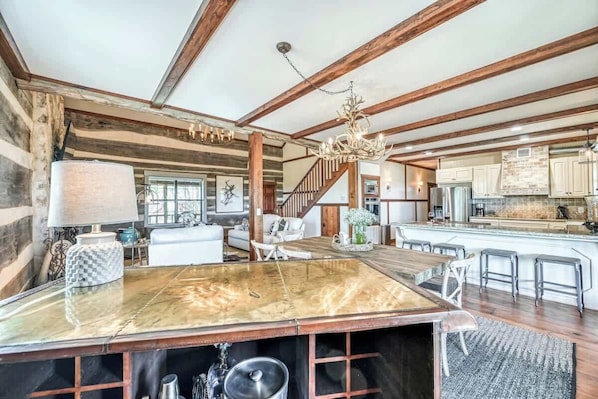 A spacious kitchen with a large island, wooden beams, and a chandelier.