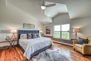 A bedroom with a large bed, a ceiling fan, a window with a view, and a leather armchair. - Lux Ranch w/Hottub|AlamoSprings (Fredericksburg)