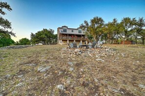 A two-story building with a balcony, surrounded by a rocky landscape and trees. - Lux Ranch w/Hottub|AlamoSprings (Fredericksburg)