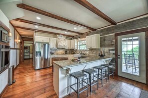 A spacious kitchen with a large island, wooden beams, and a view of the outdoors. - Lux Ranch w/Hottub|AlamoSprings (Fredericksburg)