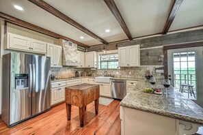 A kitchen with wooden beams, a stainless steel refrigerator, granite countertops, and a stone backsplash.