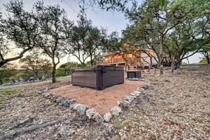 A rustic cabin with a stone fireplace, surrounded by trees and a stone border. - Lux Ranch w/Hottub|AlamoSprings (Fredericksburg)