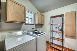 A laundry area with a washing machine, dryer, wooden cabinets, and a metal shelving unit. - Lux Ranch w/Hottub|AlamoSprings (Fredericksburg)