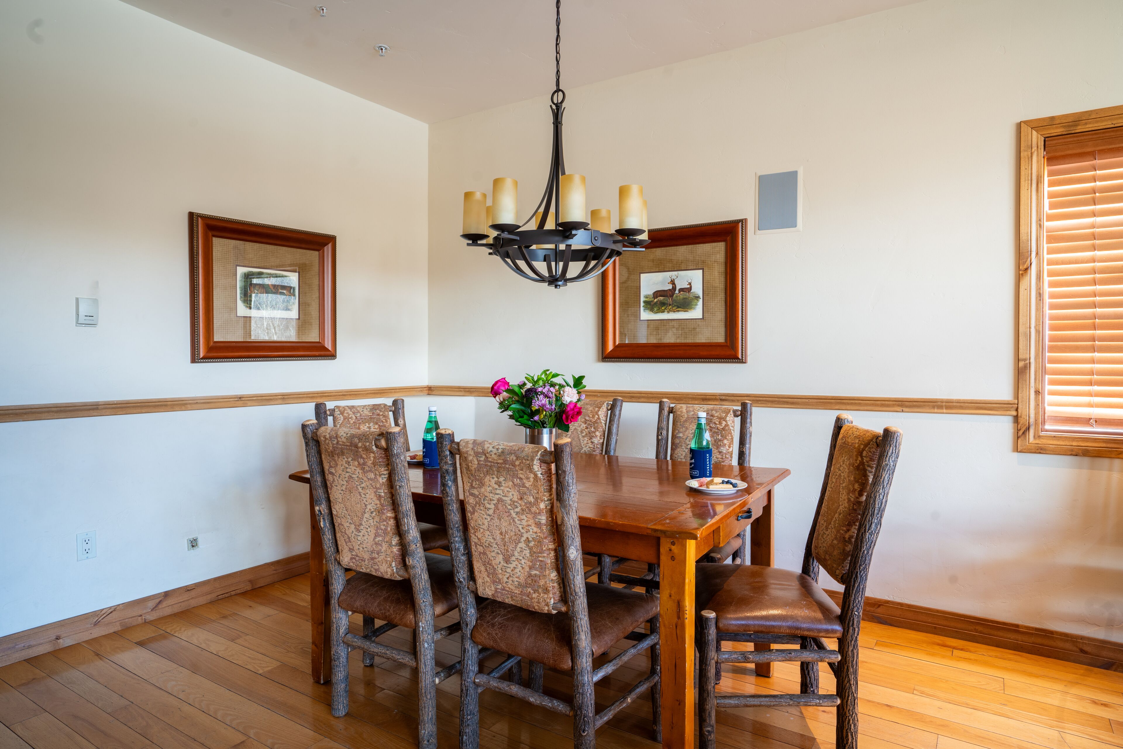 A dining area with a wooden table and chairs, framed pictures on the walls, and a chandelier.