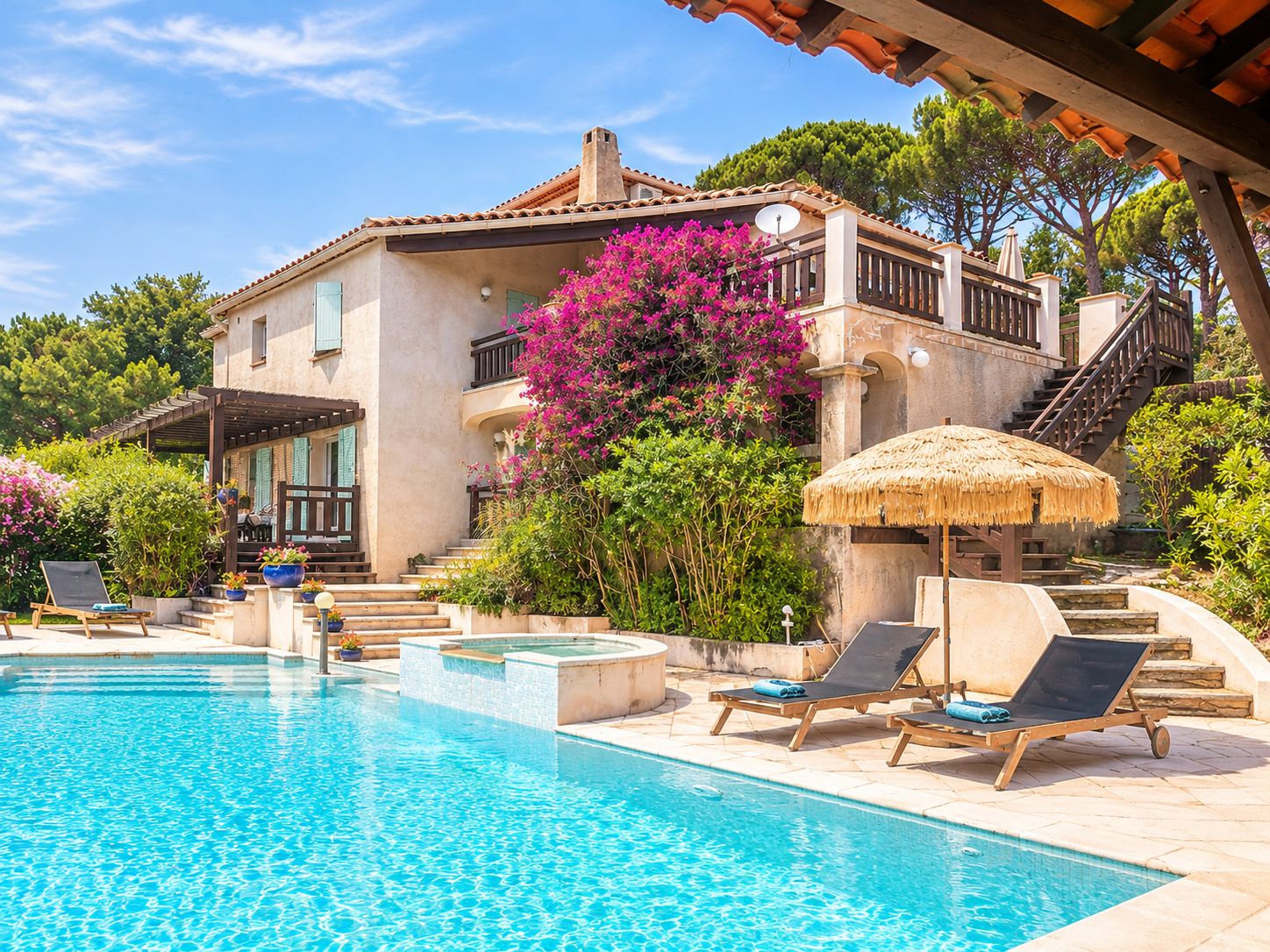 A poolside area with lounge chairs, a thatched umbrella, and a staircase leading to a building with a tiled roof.