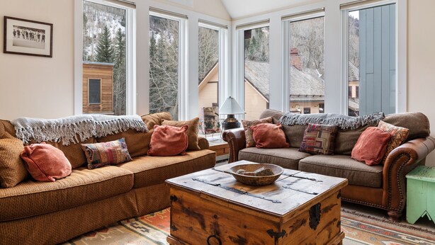 A cozy living room with two brown sofas, a wooden coffee table, and large windows offering a view of a snowy mountain. - Legacy House by AvantStay | Beautiful 4BDR Home in Great Location w/ Hot Tub (Telluride)