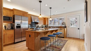 A modern kitchen with wooden cabinets, stainless steel appliances, and a central island with bar stools. - Legacy House by AvantStay | Beautiful 4BDR Home in Great Location w/ Hot Tub (Telluride)