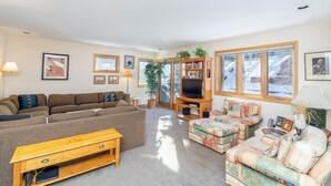 Ein Wohnzimmer mit einem großzügigen Ecksofa, einem kleinen Sofa, einem Holztisch und einem Fernseher auf einem Holzschrank.