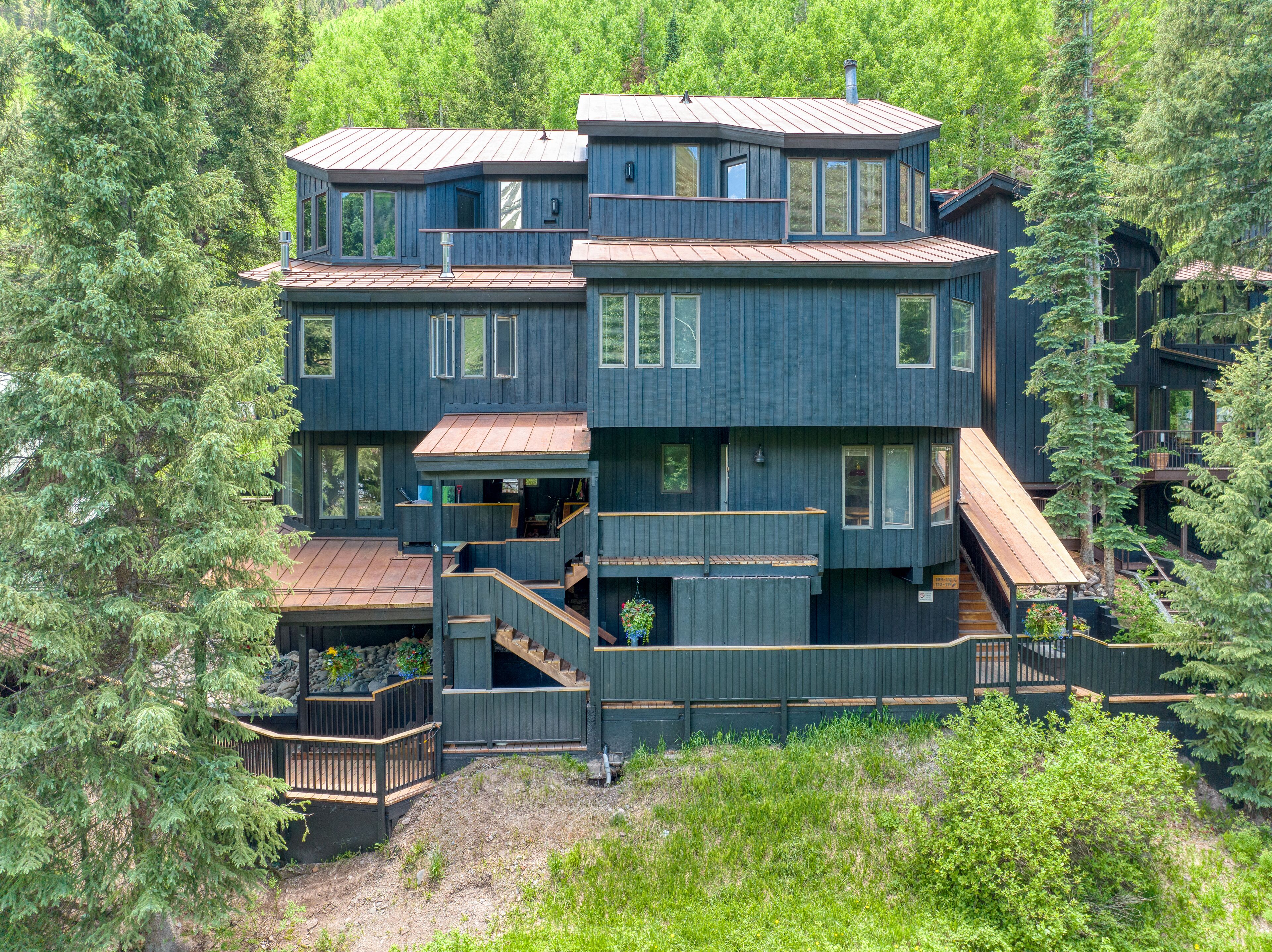 Une cabane en bois à plusieurs étages, dotée d’un balcon et entourée d’une forêt dense.