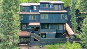 A multi-story wooden cabin with a balcony, surrounded by dense forest.