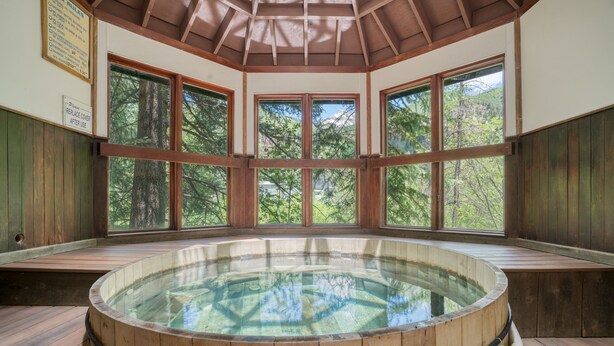 A wooden hot tub with a glass bottom, surrounded by large windows offering a view of trees.