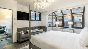 A modern bedroom with a large bed, a grey sofa, a TV, and a chandelier.