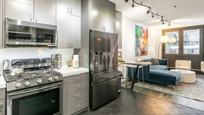 A modern kitchen with stainless steel appliances, a dining area with a blue sofa, and a large window providing natural light.