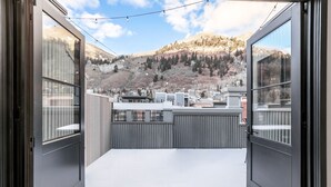 A balcony with a view of a mountainous landscape, a metal railing, and a clear sky.