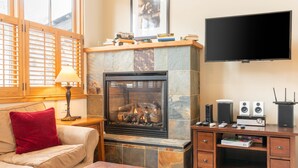 Una sala de estar con chimenea, un sofá, un televisor y un mueble de madera para entretenimiento con altavoces.