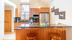 Una cocina con armarios de madera, una isla grande con taburetes de bar, un refrigerador y una ventana con persianas.