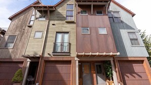 Un edificio residencial de varios pisos con revestimiento de madera y metal, múltiples ventanas y una entrada con portón.