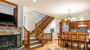 Un vaste espace de vie doté d’une cheminée, d’un escalier en bois et d’un coin repas avec des chaises et une table en bois.