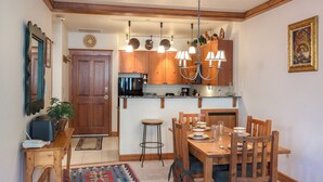 Ein Essbereich mit Holztisch und -stühlen, eine Küche mit Holzausstattung und einer integrierten Kochinsel, darüber ein Kronleuchter.
